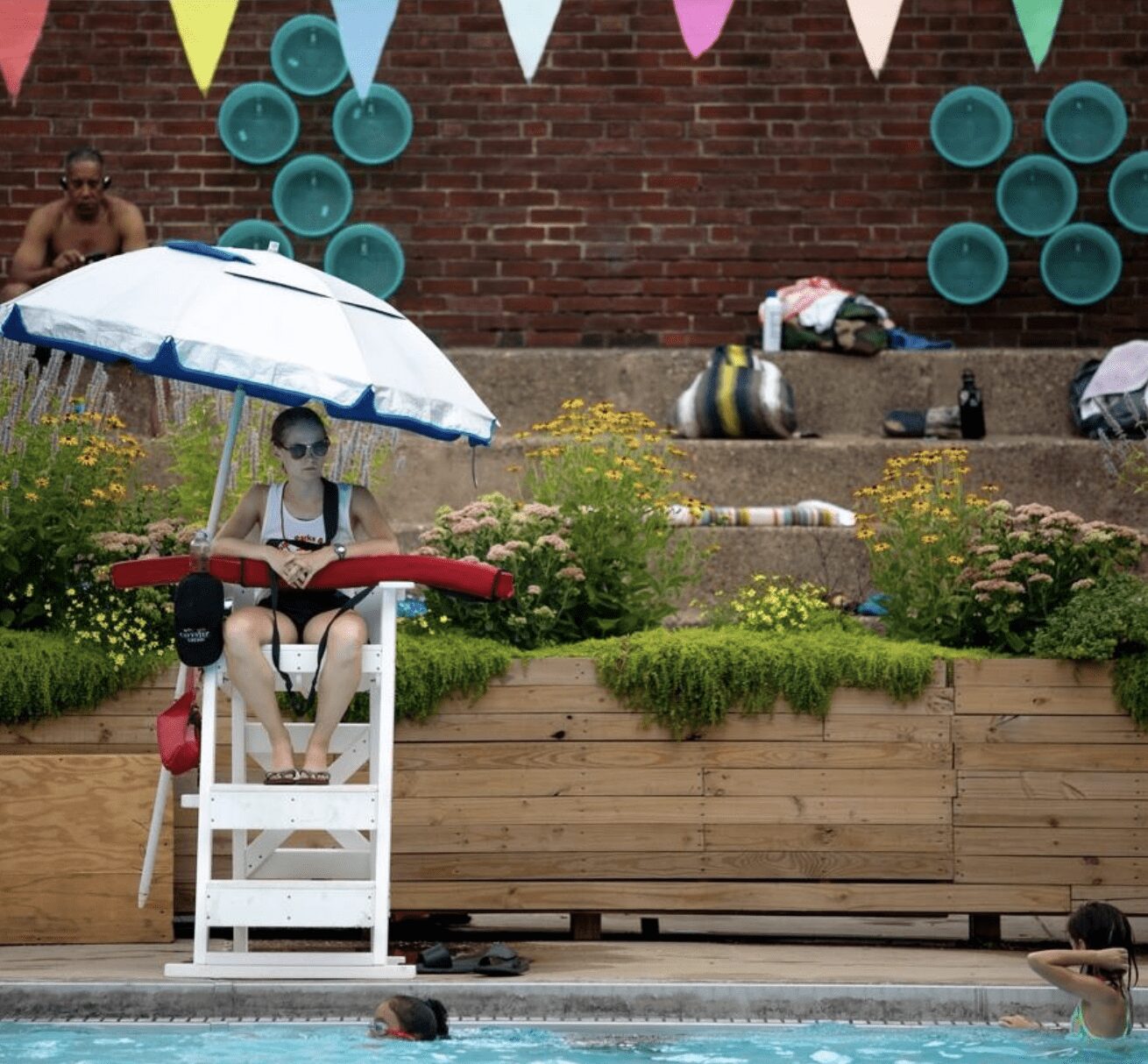 A young woman sitting in a lifeguard chair at an outdoor pool