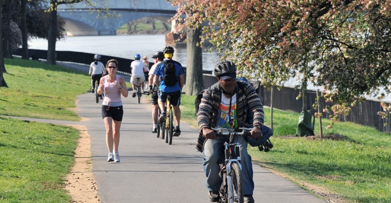 Many people biking, walking, and running on a paved trail on a waterfront park
