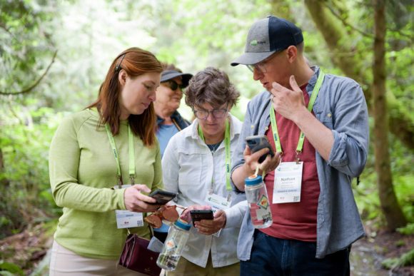 Three Greater & Greener attendees looking at their phones together at an outdoor session