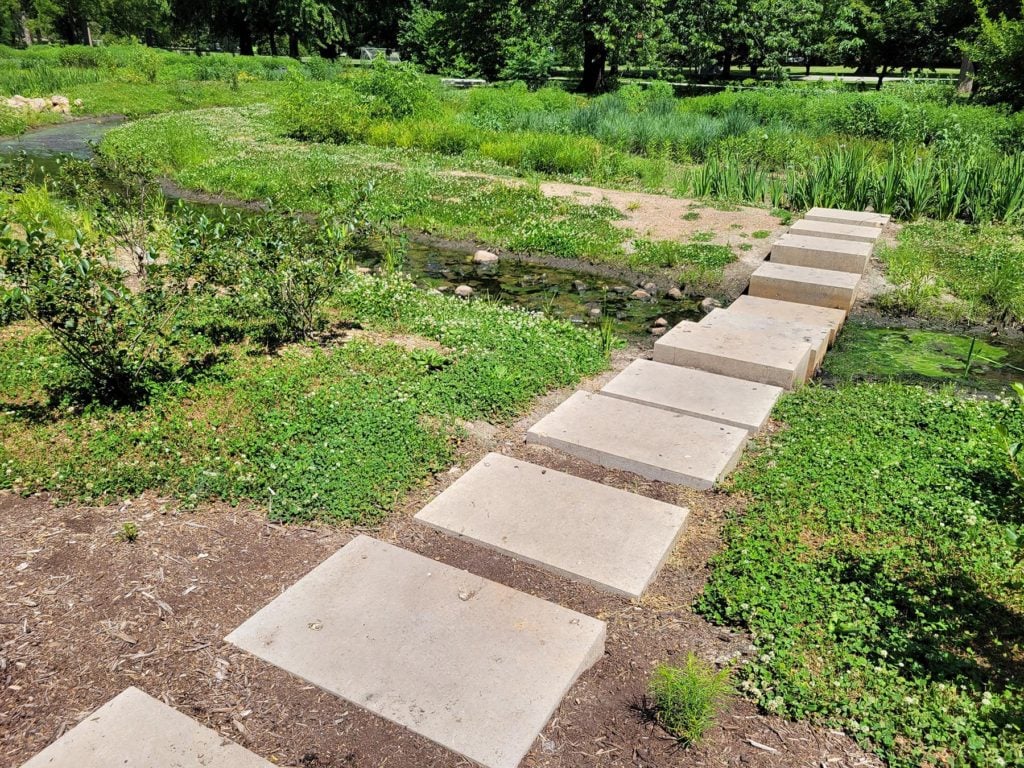 A lush green park with concrete pavers going across a small creek