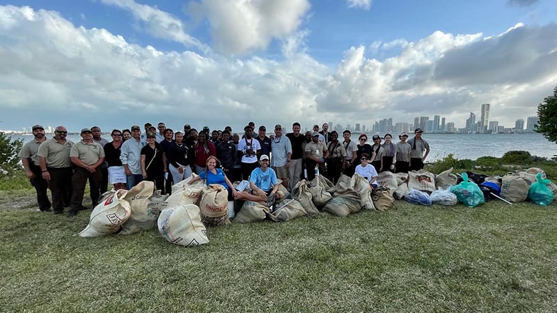 Group of people standing behind bags of trash. The Miami skyline is in the background.