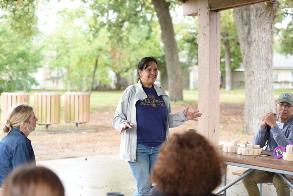 Picture of a woman presenting to a group of people outside.