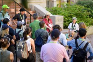 A large group of people listening to a speaker outside in front of steps