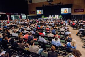 A large crowd listening to a person speak in an event hall