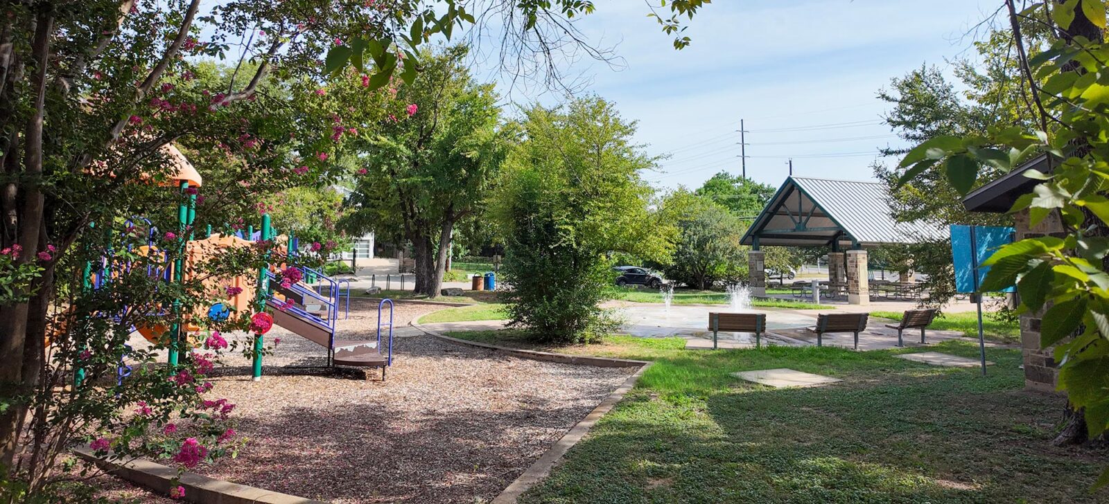 A park with a playground, benches, pavilion, and water feature