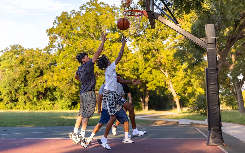 Young teen boys laying up a basketball at an outdoor court in a park