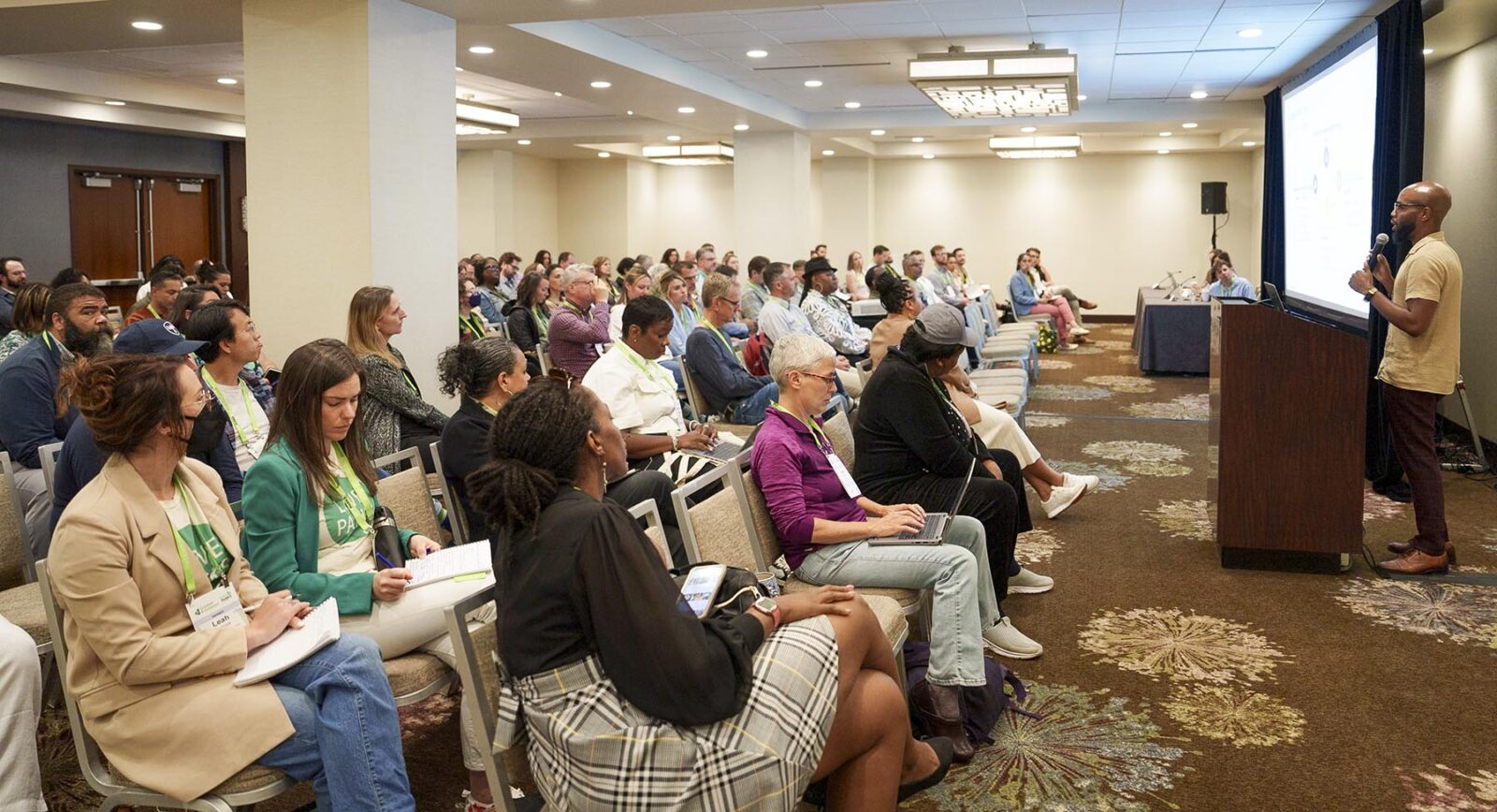 A large group listening to a presentation in a hotel conference room