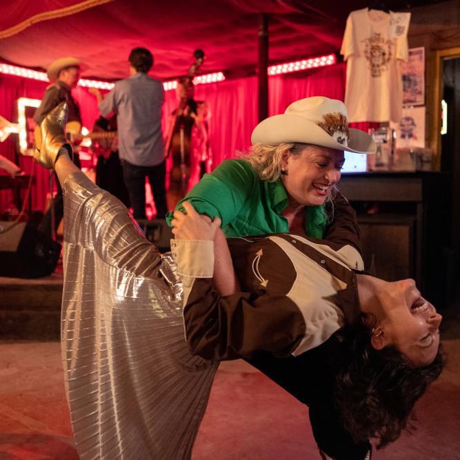 Two women in cowboy outfits dancing in a bar