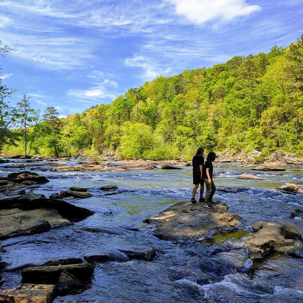 Two people standing on a rock in a large creek