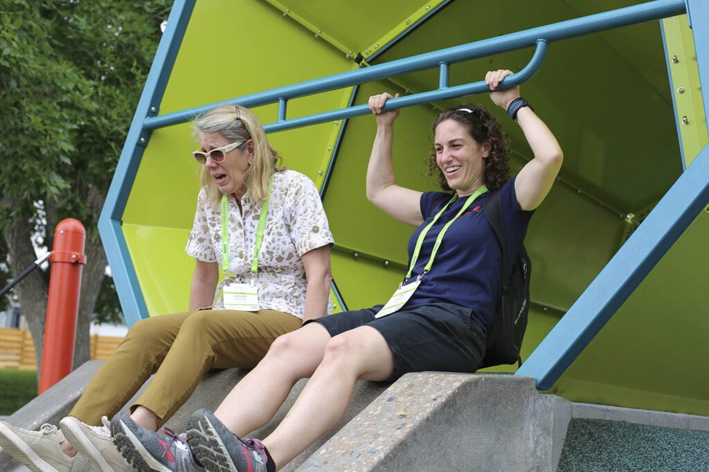 Two women sitting at the top of a large slide