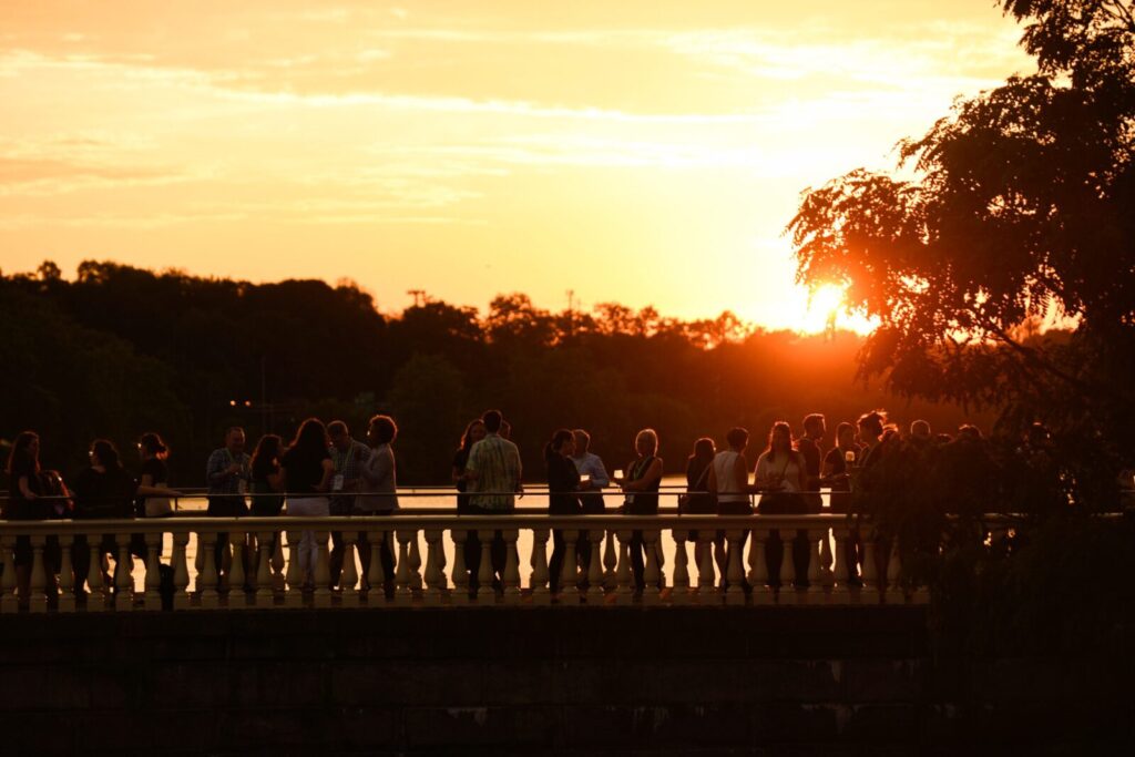 A large group of people mingling in front of a sunset