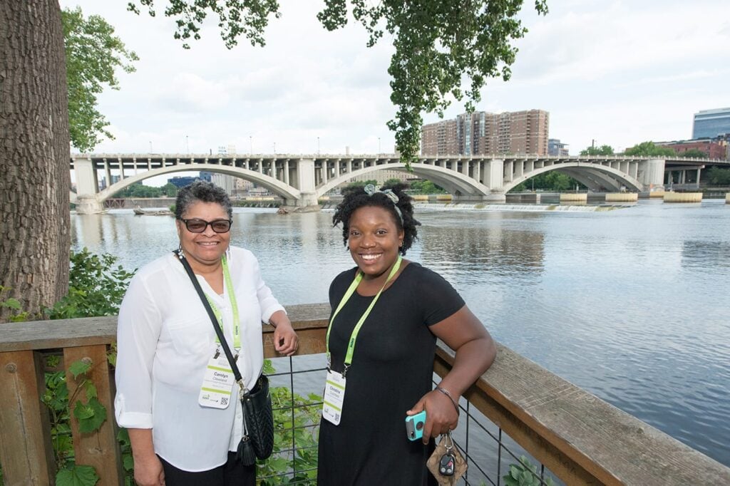 Two woman posing in front of a bridge and waterway