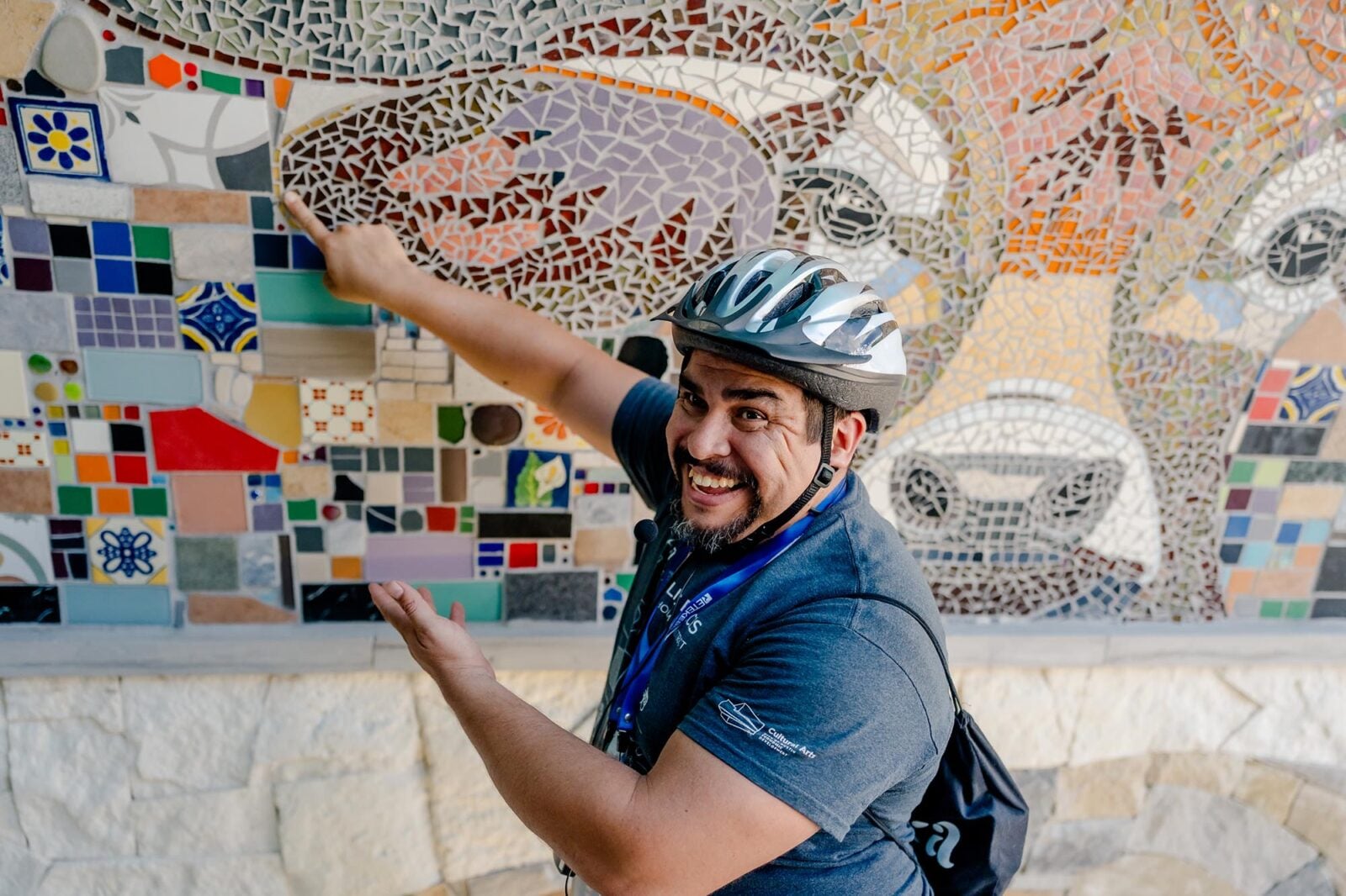 A man in a bike helmet pointing to a wall mosaic
