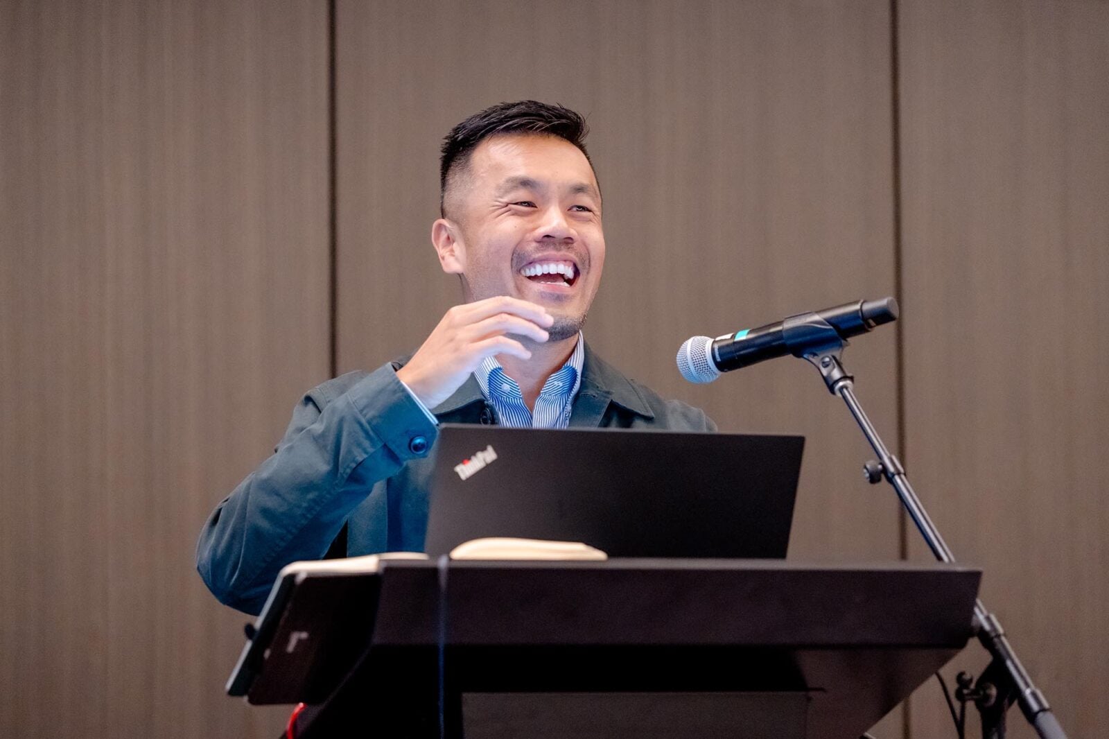 A man smiling in front of a computer and microphone