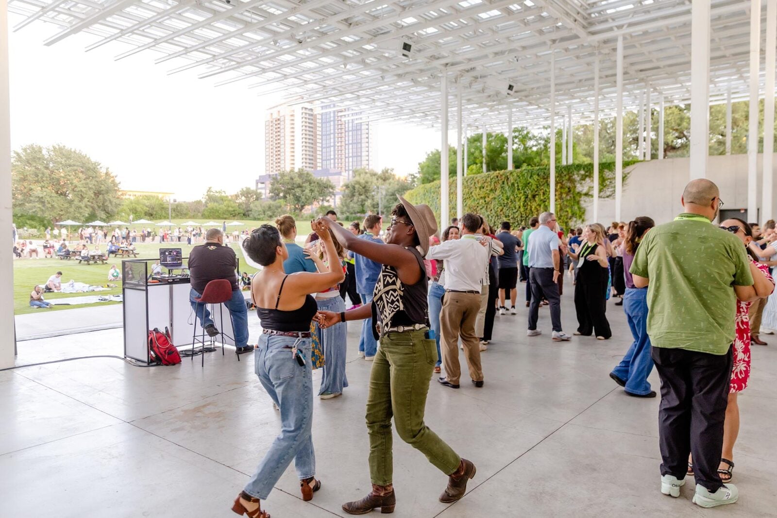 A large group doing a Texas two-step lesson under a park awning