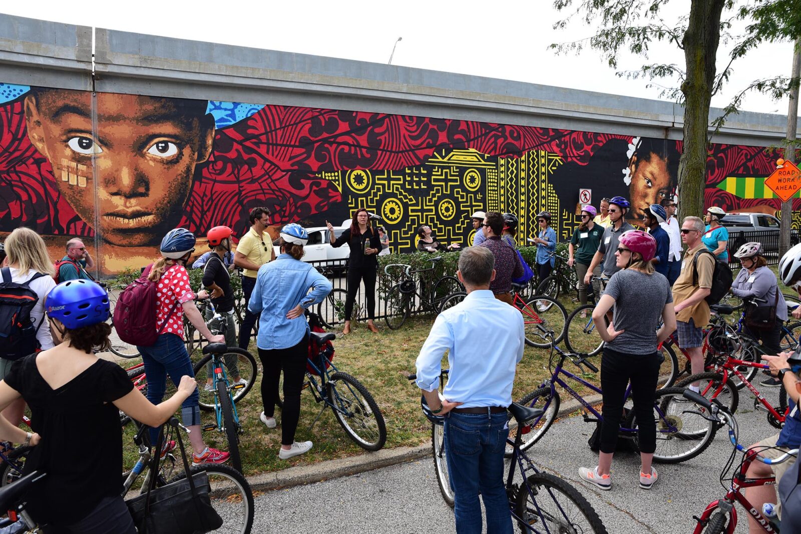 Park Study Tour attendees with bikes listening to a tour leader at a city mural